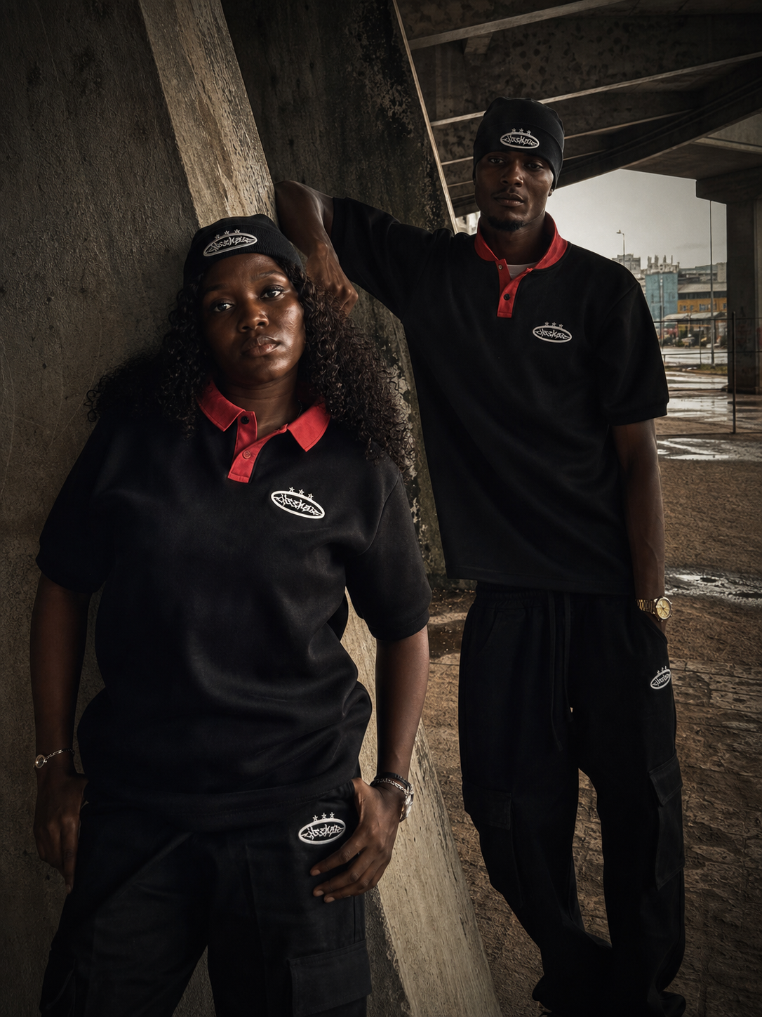 Two ENSEMBLE models in black polo streetwear under a Lagos concrete bridge